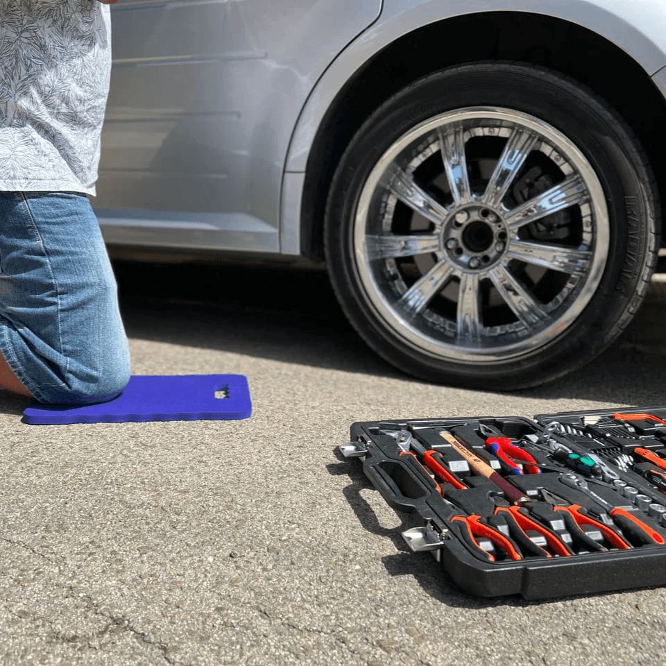 Ein Mechaniker kniet neben einem Auto und verwendet Werkzeuge aus einem schwarzen Werkzeugkasten.