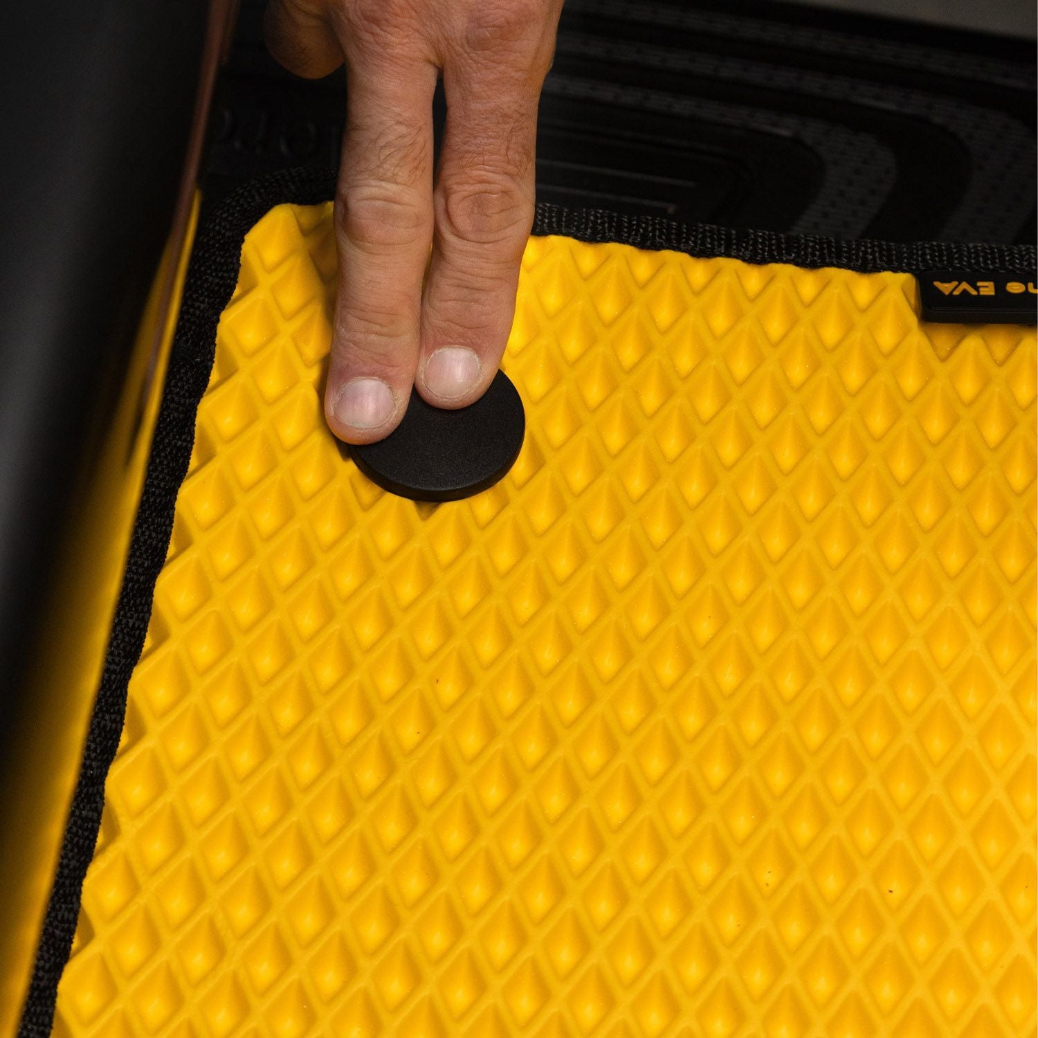 Gelber EVA-Autoteppich mit rautenförmigem Muster und einer Hand, die ihn fixiert.