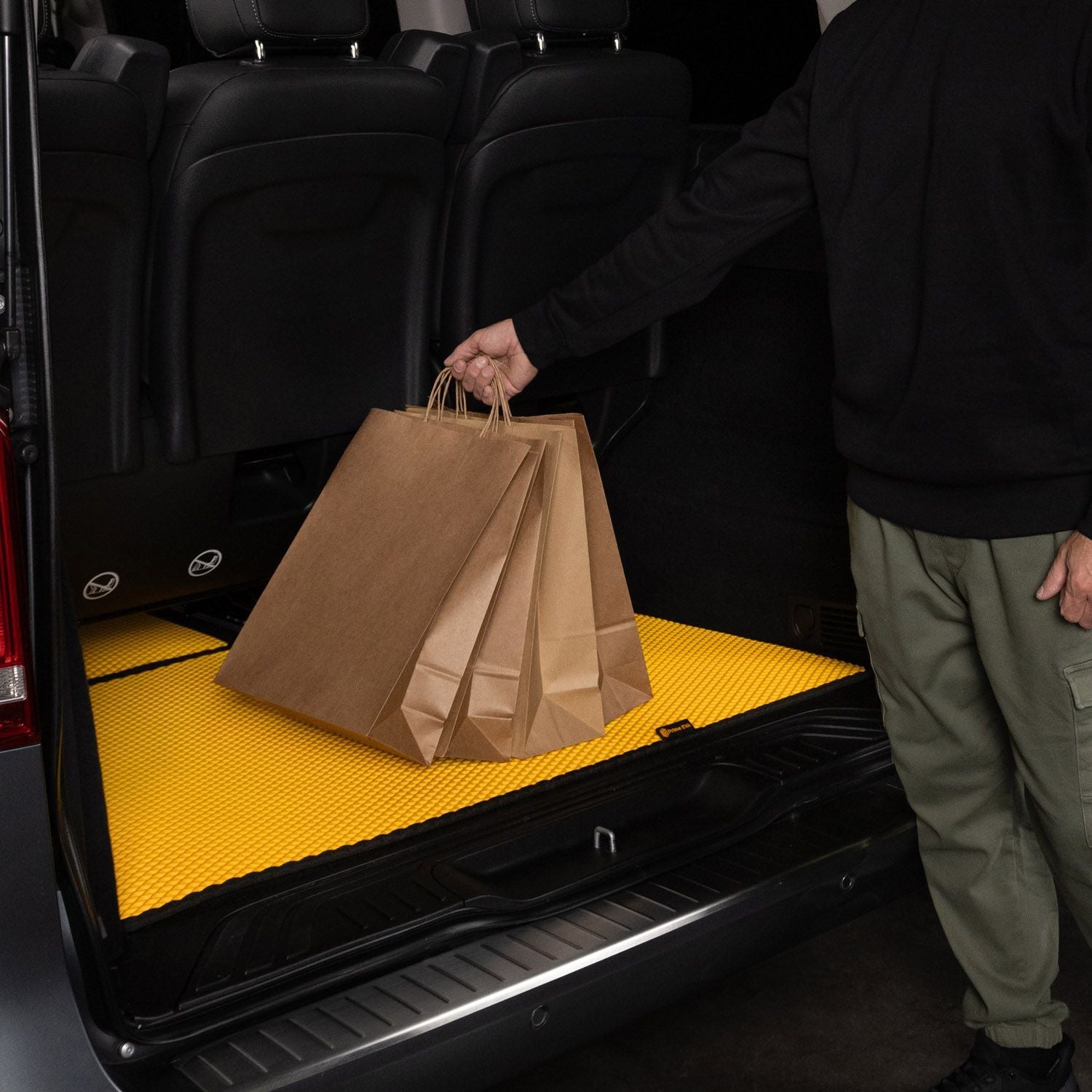 Gelbe EVA-Autoteppich-Bodenmatte mit Kofferraumschutz und Papiertüten im Hintergrund.