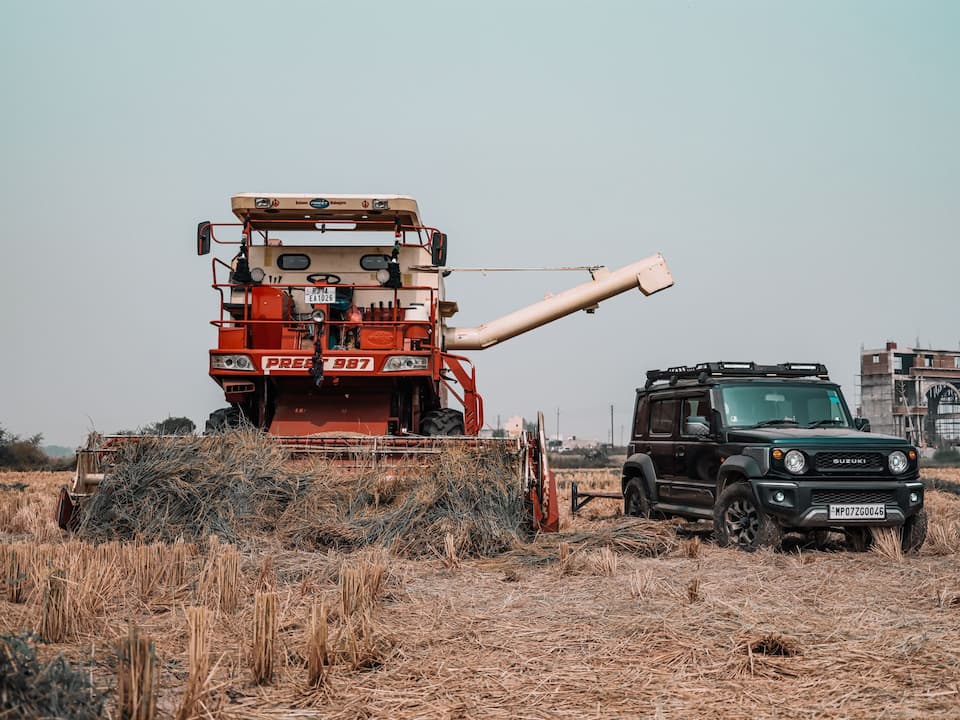 Auto neben einer Landmaschine auf einem landwirtschaftlichen Feld.