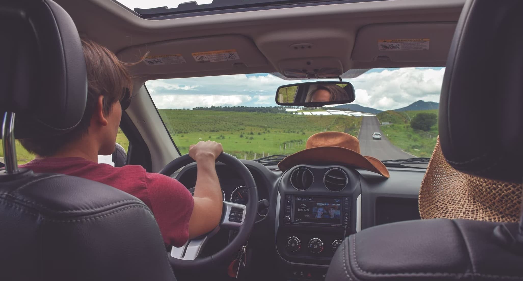 Blick vom Rücksitz auf Fahrer bei landschaftlicher Autofahrt im modernen Auto mit offenem Dach.