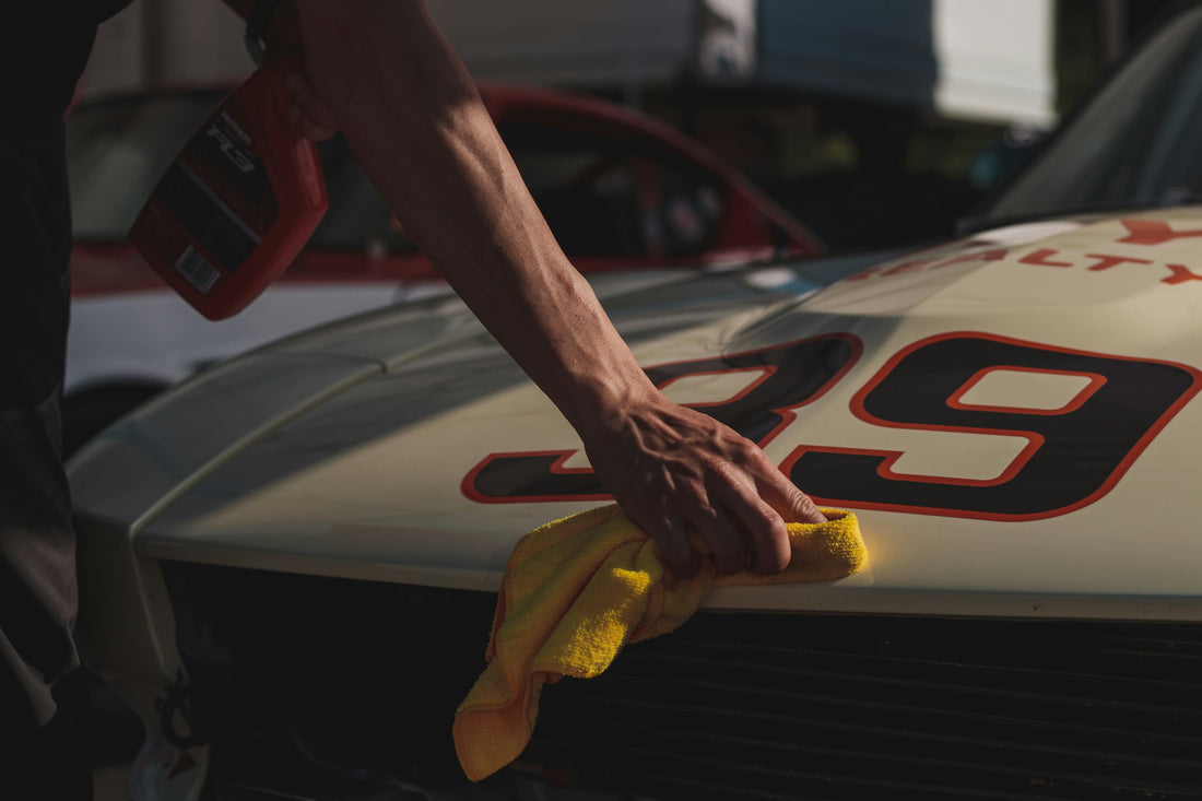 Hand poliert die Motorhaube eines Rennwagens mit gelbem Tuch und Pflegespray