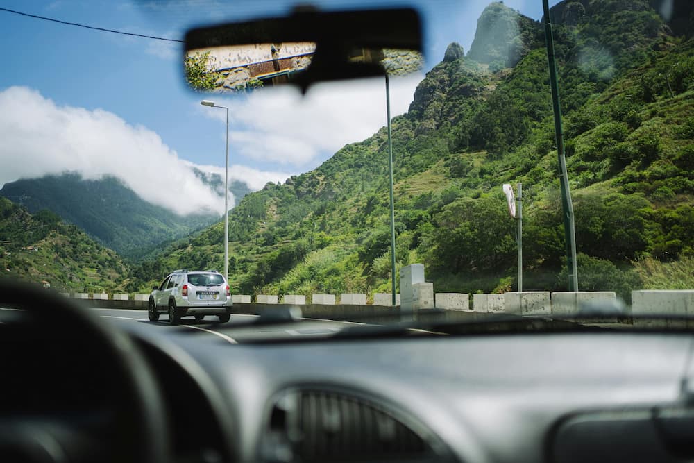 Blick aus dem Auto auf Bergstraße mit Landschaft und vorausfahrendem Fahrzeug.