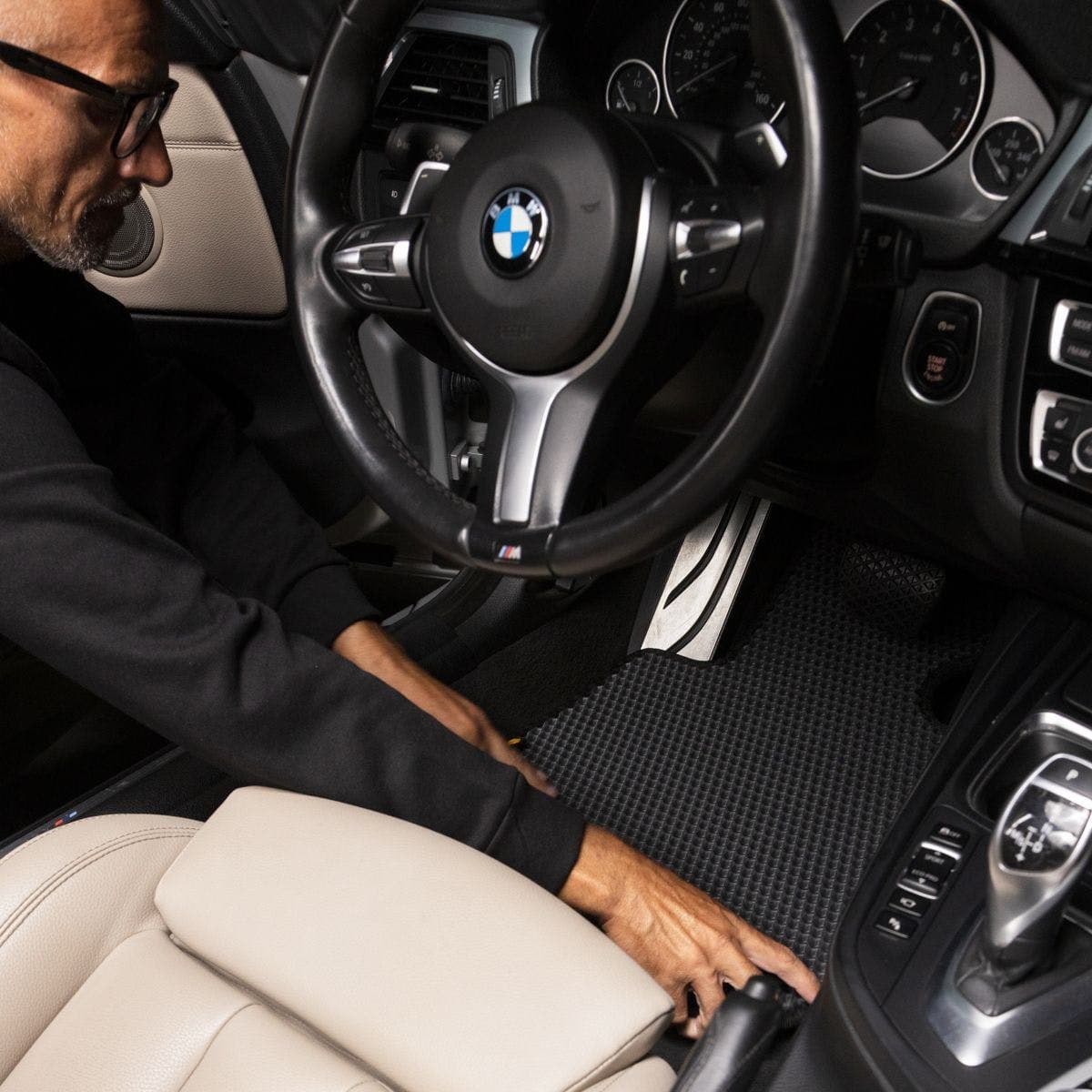 Fahrer montiert EVA-Autofußmatte im BMW mit schwarzem und beigem Lederinterieur.