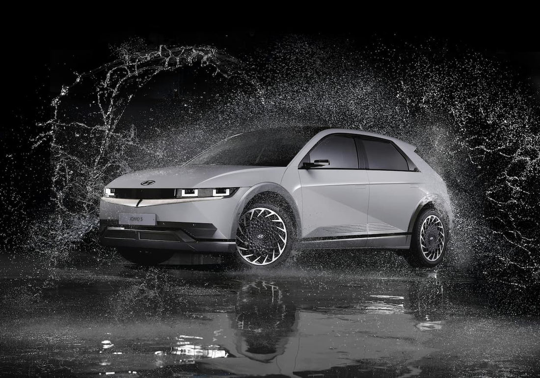 Elektroauto faehrt nachts durch einen grossen Wasserspritzer und erzeugt dynamische Bewegung auf nasser Fahrbahn.