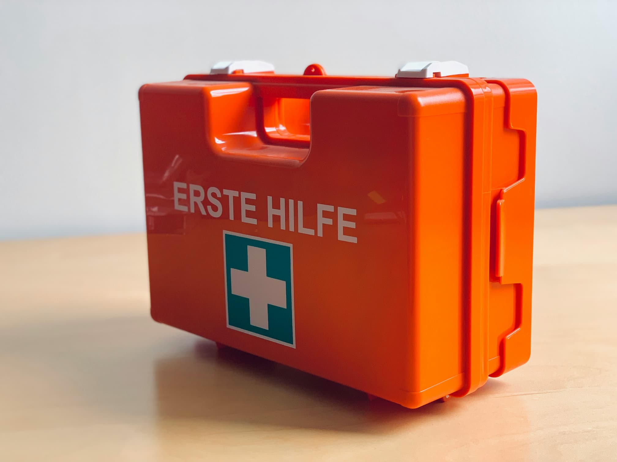 Oranger Erste-Hilfe-Kasten mit Beschriftung auf einem Holztisch.