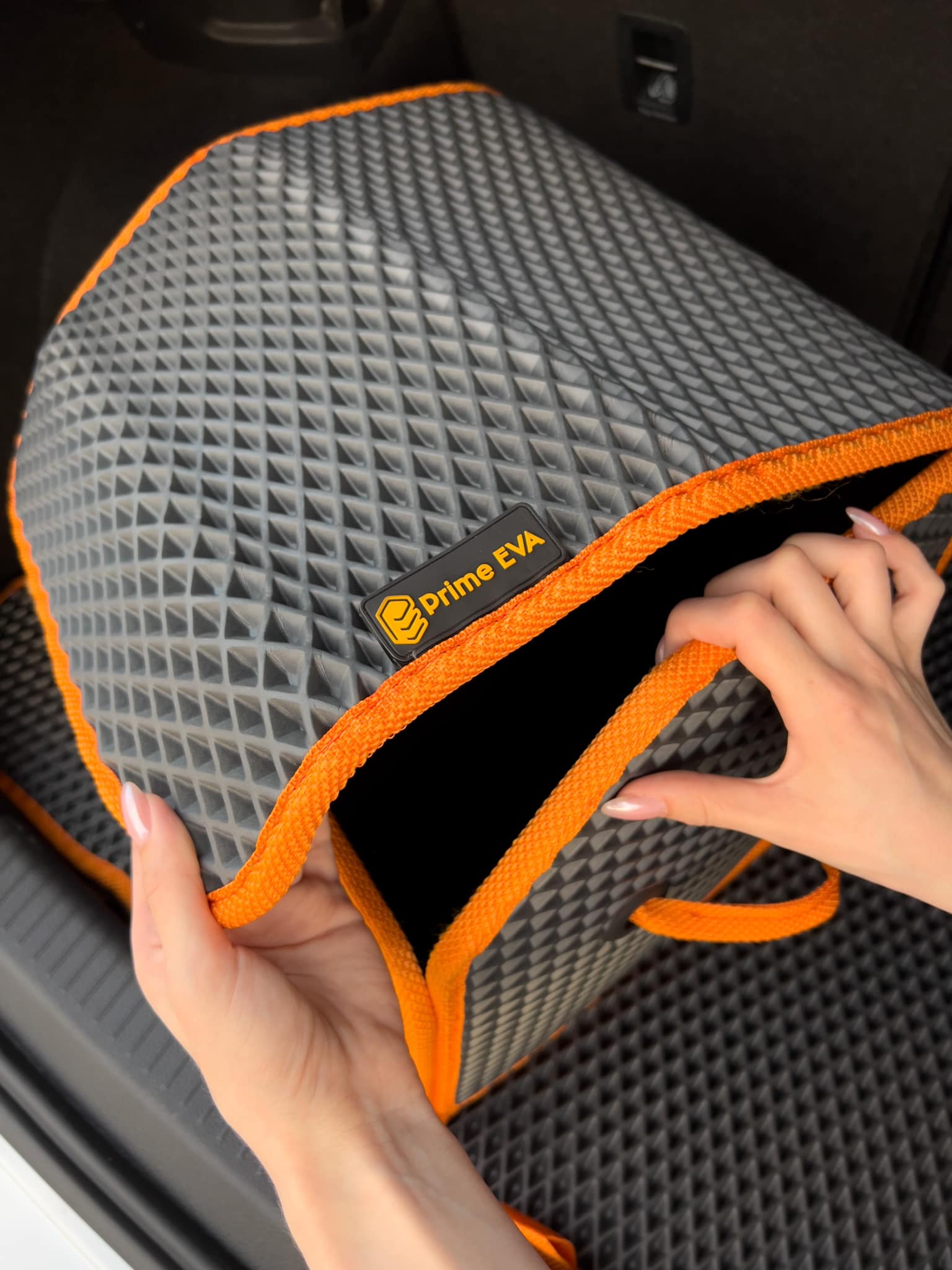 Hände halten einen maßgefertigten EVA-Auto-Organizer mit orangem Rand im Kofferraum eines Autos.