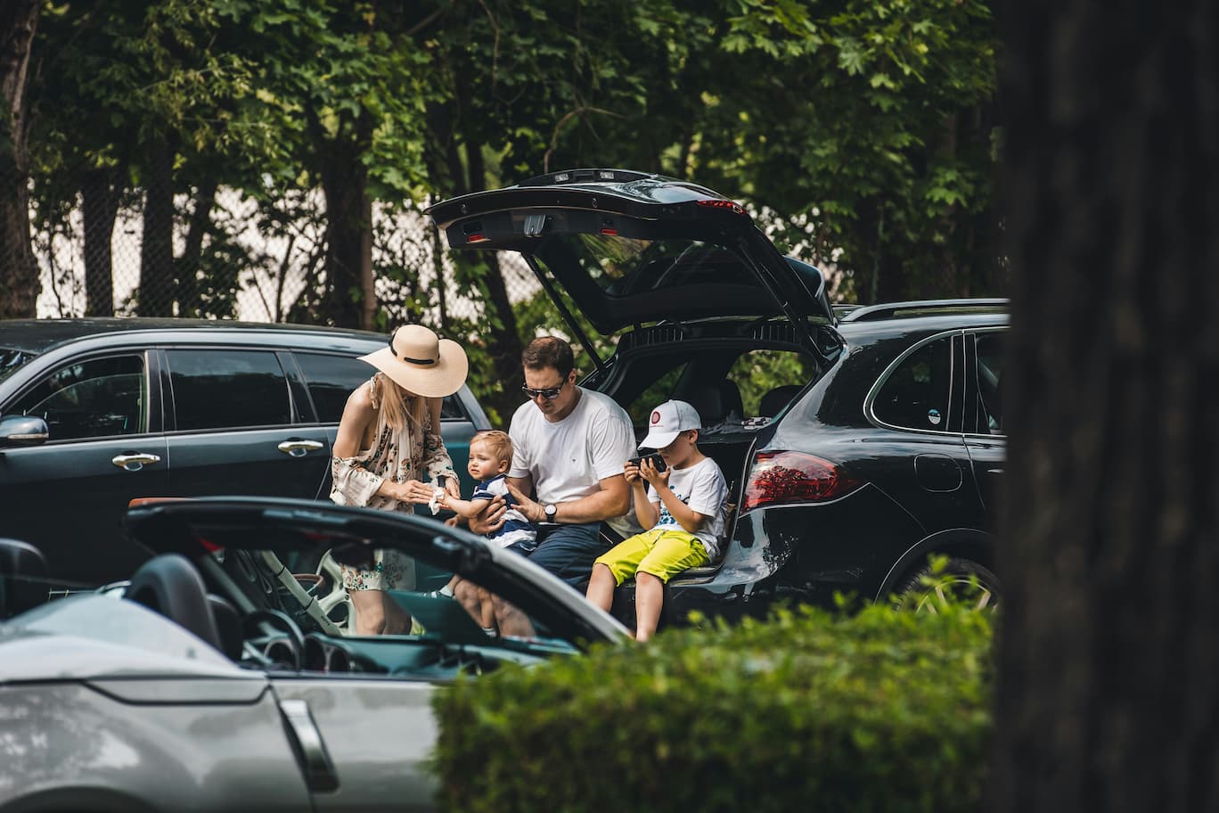 Familie macht Picknick und nutzt den offenen Autokofferraum als Sitzplatz während eines Ausflugs.