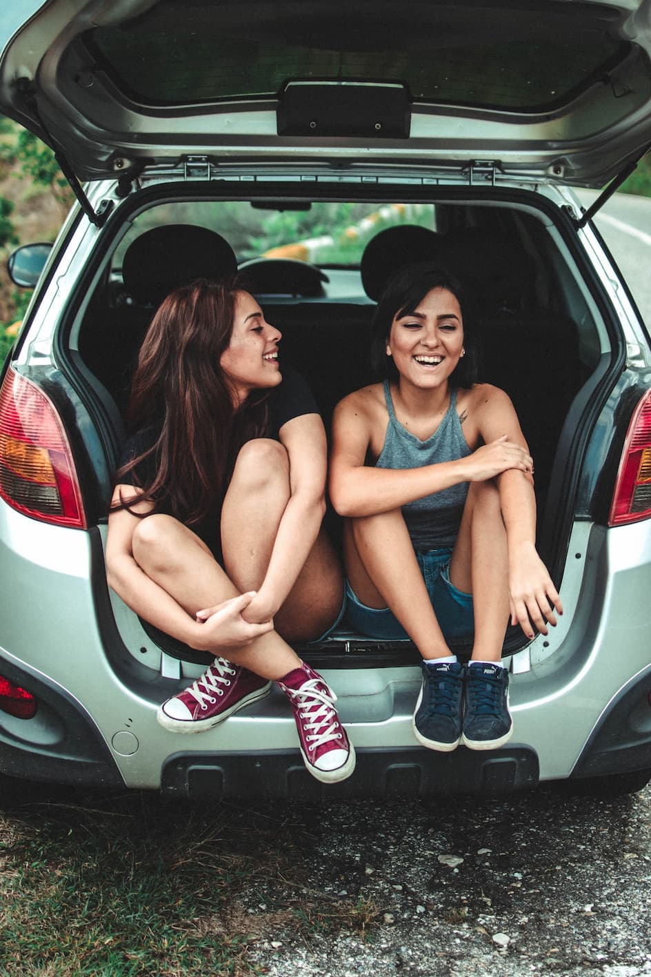 Zwei Frauen sitzen im offenen Kofferraum eines Autos, lachen und genießen den Moment