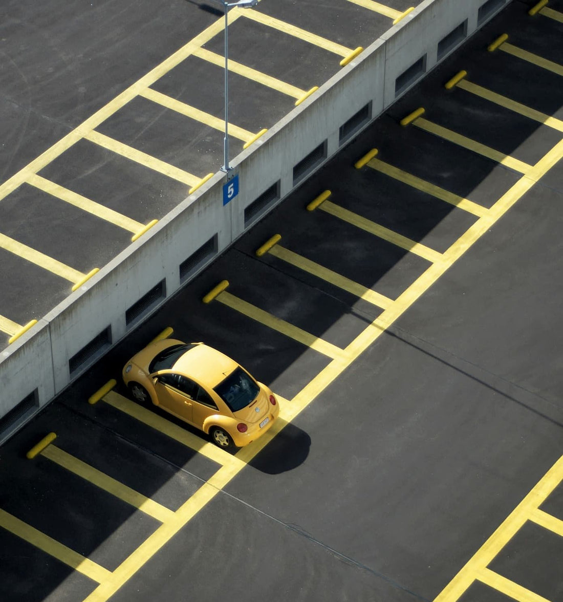 Gelbes Kompaktfahrzeug allein auf leerem, markiertem Parkplatz geparkt.