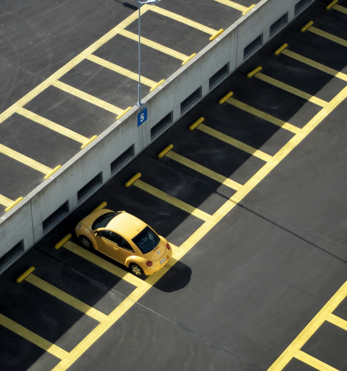 Gelbes Kompaktfahrzeug allein auf leerem, markiertem Parkplatz geparkt.