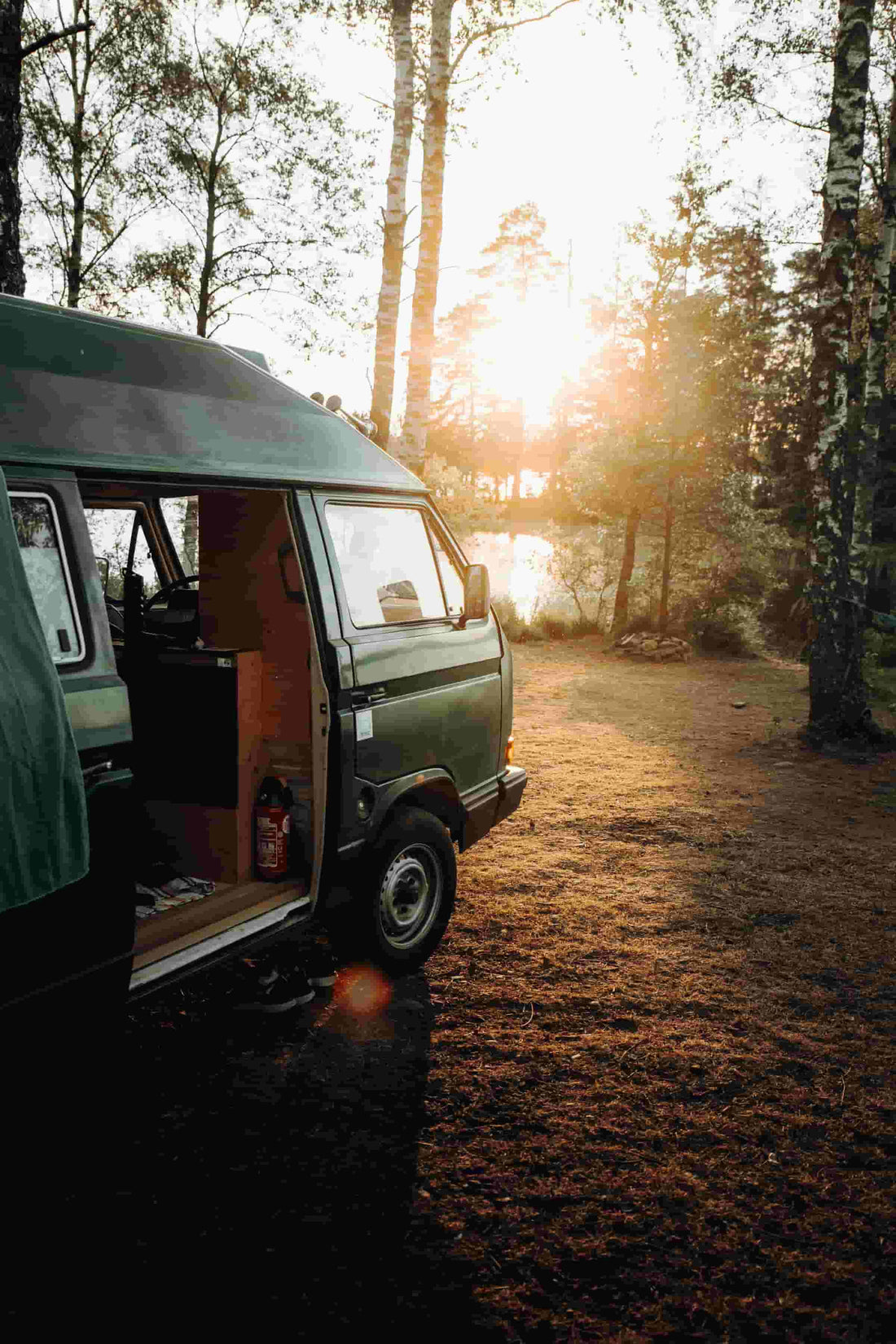 Grüner Campingbus am Waldsee bei Sonnenuntergang.