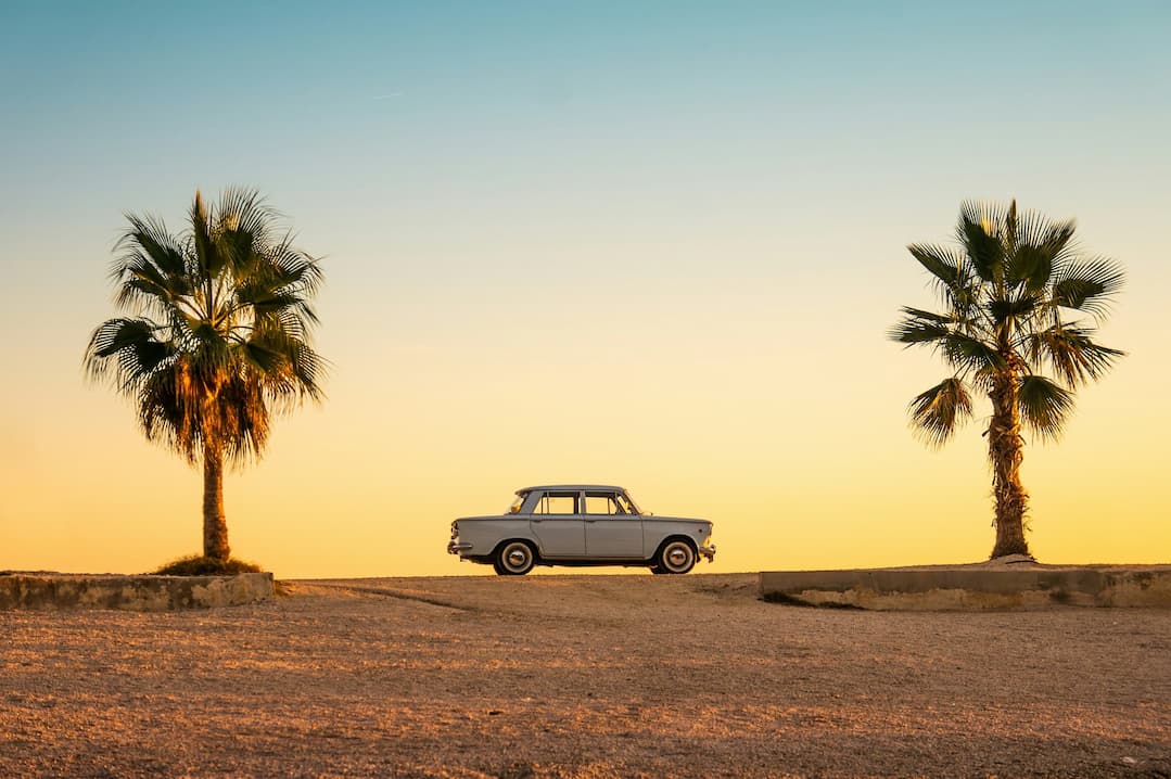 Klassisches Vintage-Auto zwischen Palmen bei Sonnenuntergang.