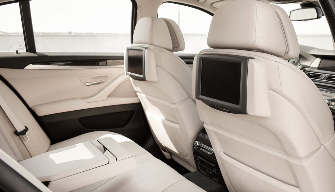Luxusauto-Innenraum mit beigen Ledersitzen und Entertainment-Bildschirmen an den Rückenlehnen.