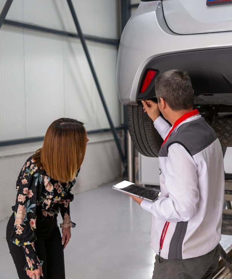 Mechaniker prüft mit einer Kundin das Hinterrad eines Autos.