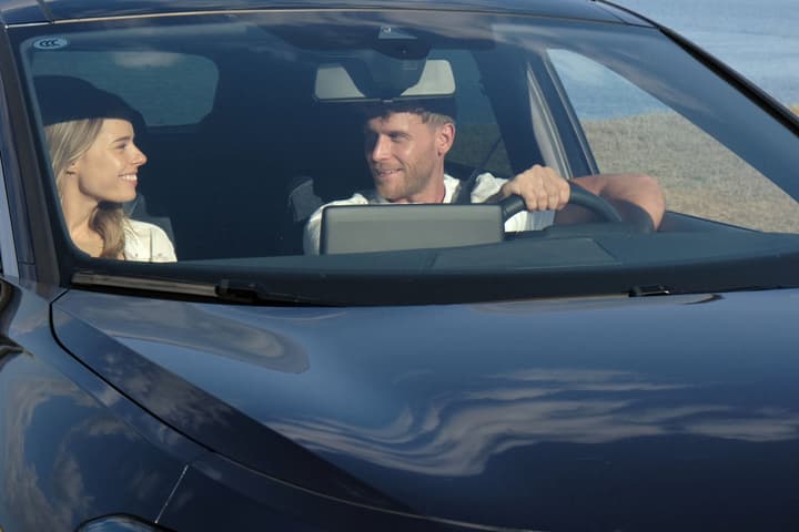Lachendes Paar sitzt in einem modernen Auto, durch die Windschutzscheibe gesehen.