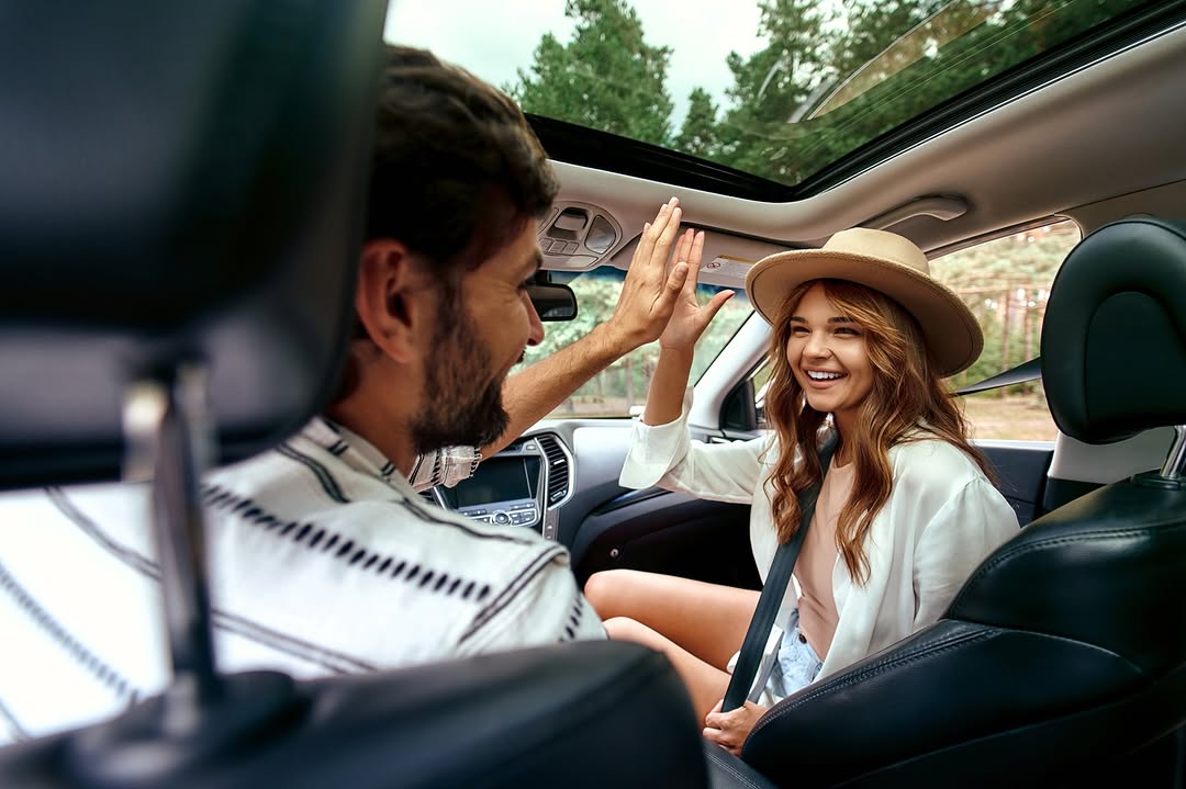 Ein glückliches Paar genießt eine Autofahrt, die Frau lächelt und gibt dem Mann einen High Five.