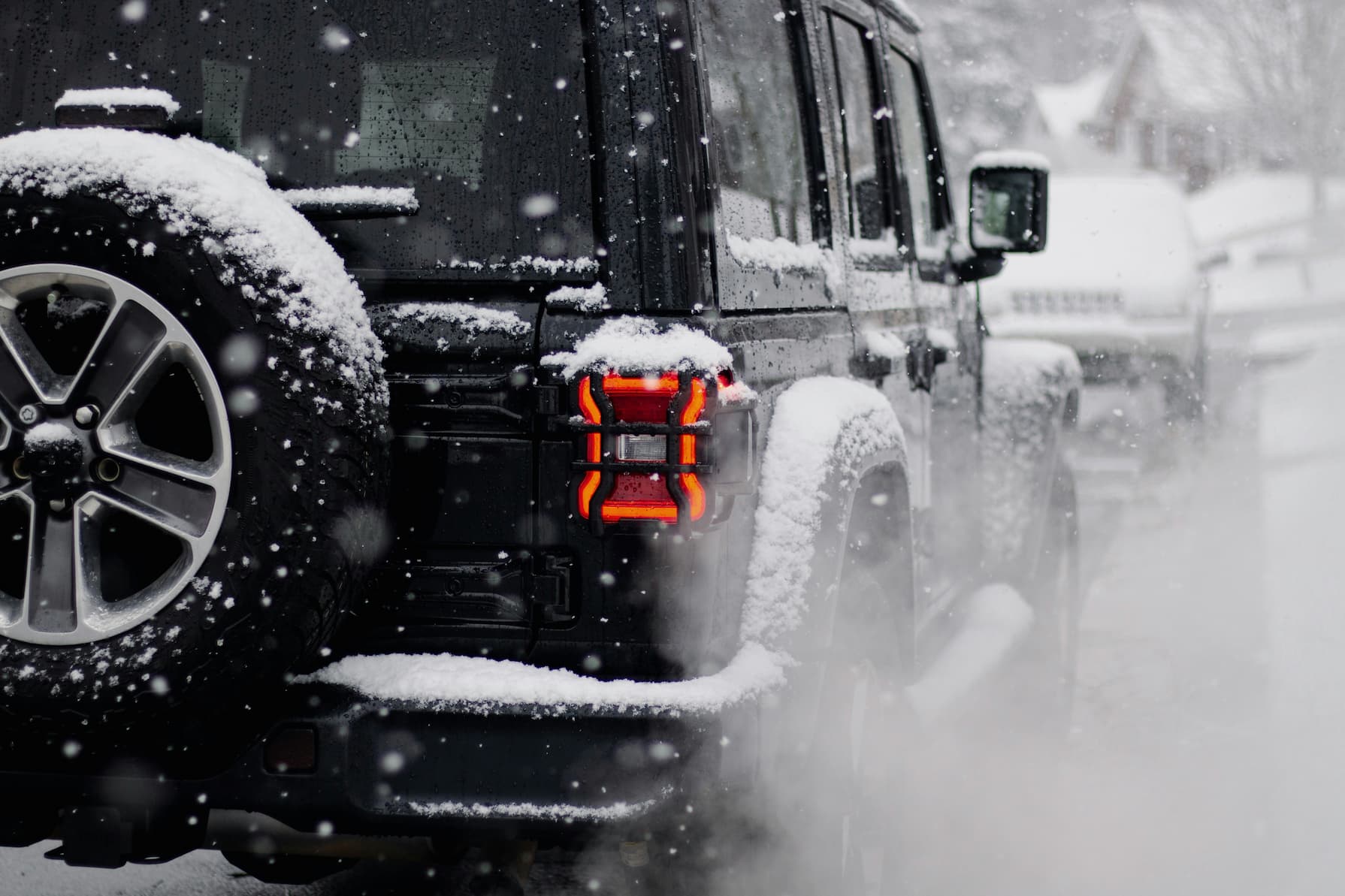 Schwarzer SUV fährt auf schneebedeckter Straße mit Schnee auf Reifen und leuchtendem Rücklicht.
