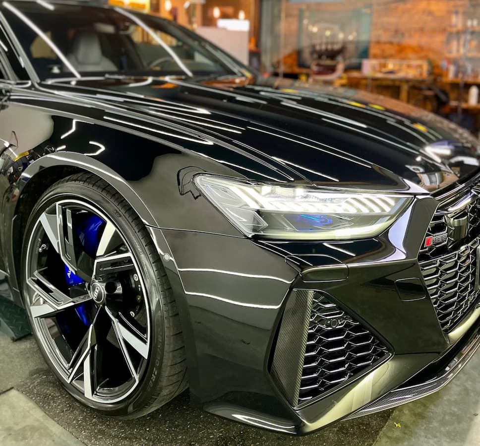 Nahaufnahme eines schwarzen Sportwagens mit polierter Karosserie und Alufelgen im Detailing-Studio.