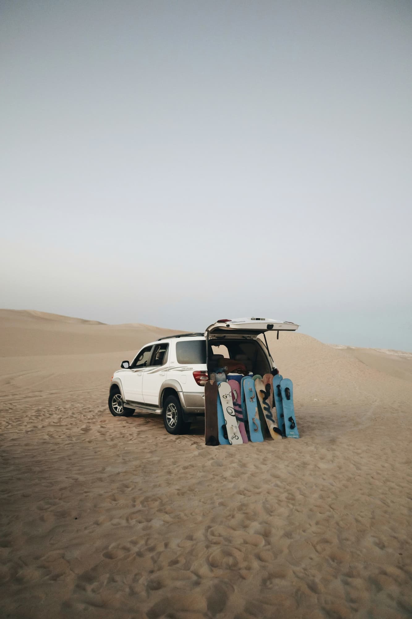 Weißer SUV auf Sanddünen geparkt mit mehreren Sandboards am geöffneten Heck.
