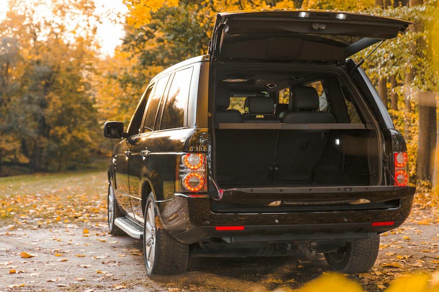 SUV mit offenem Kofferraum auf Herbstwaldweg mit gefallenen Blättern.