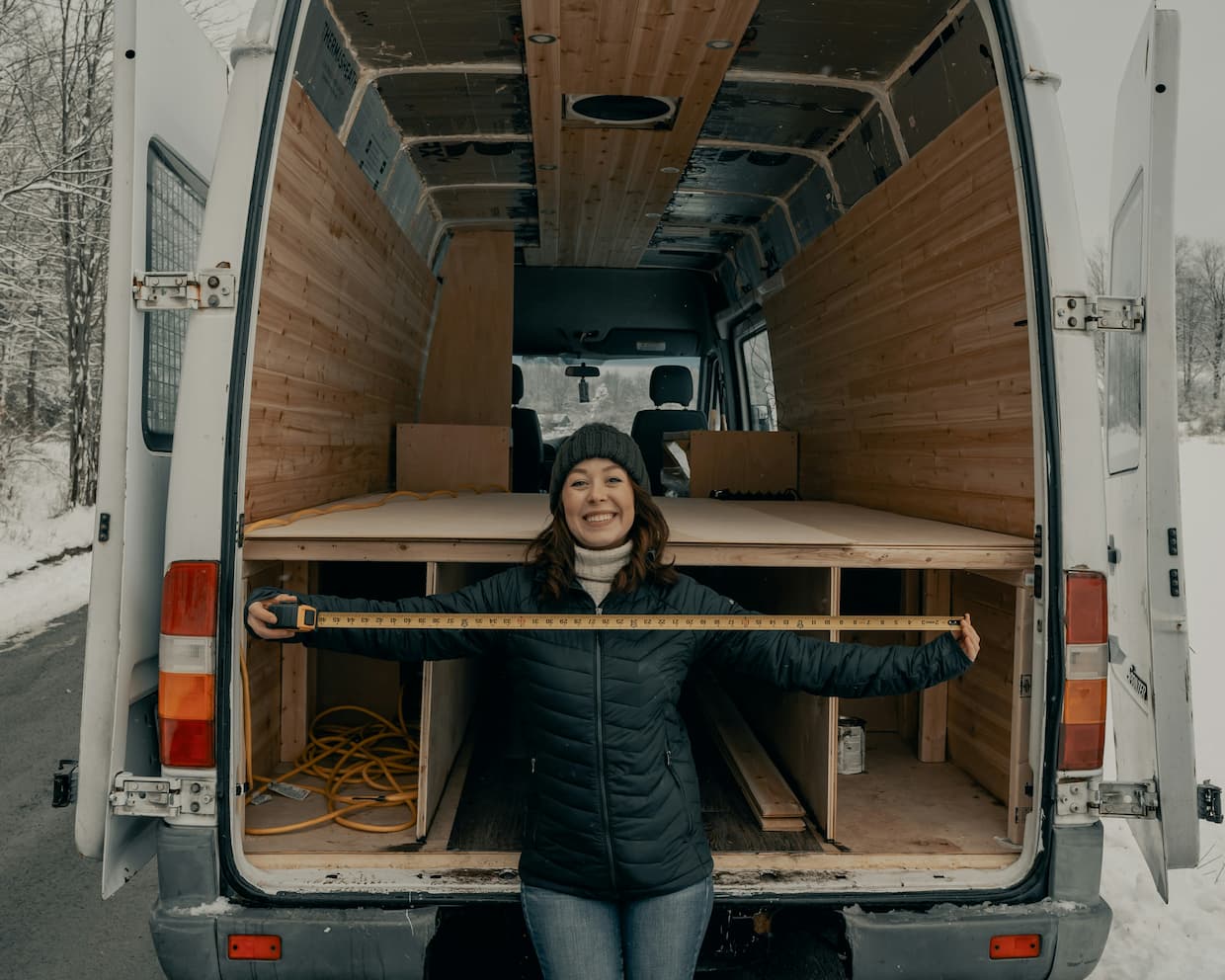 Frau misst Innenraum eines Campervans beim Ausbau mit Holzverkleidung.