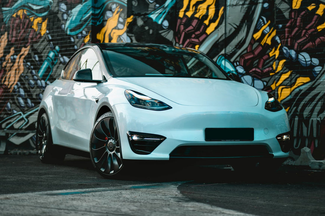Weisses Tesla Elektroauto steht in einer urbanen Umgebung vor einer bunten Graffitiwand.
