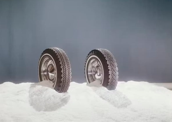 Zwei Autoreifen teilweise im Schnee vergraben, die ihr Winterprofil zeigen.