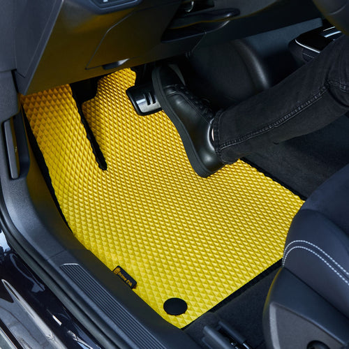 Nahaufnahme einer gelb strukturierten Autofußmatte mit einem Fuß darauf.